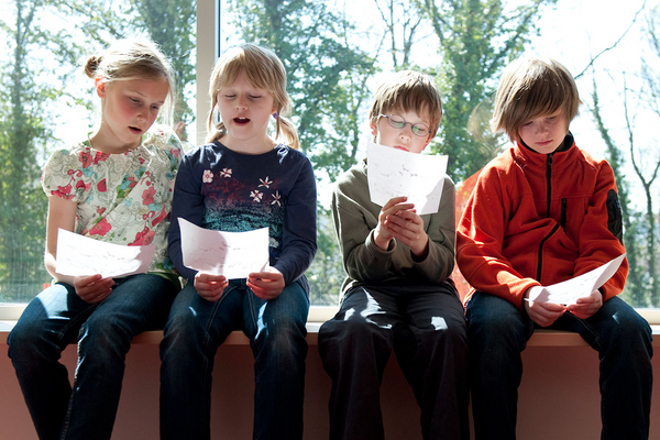 Vier Kinder sitzen auf eine Fensterbank und singen nach Noten
